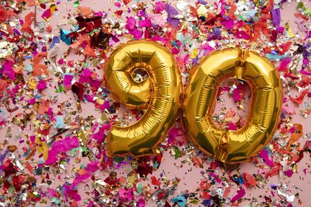 Number 90 gold birthday celebration balloon on a confetti glitter backgroundの写真素材