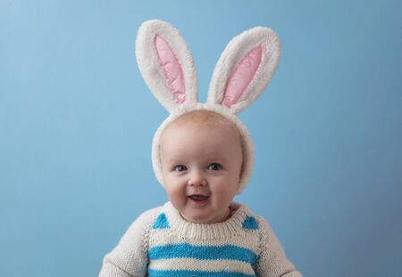 A happy baby with white easter bunny ears smiling at the camera