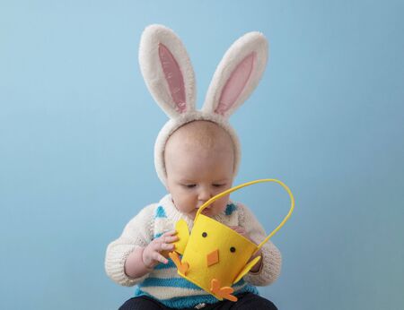 A baby wearing cute easter bunny ears peering into an easter chicken basketの写真素材