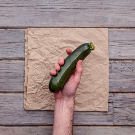 A male hand holding a fresh courgette against a rustic backgroundの写真素材