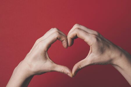 Female hands creating the shape of a love heart over a red background. Romance and valentines day conceptの写真素材
