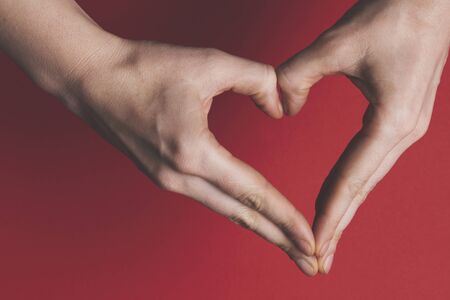 Female hands creating the shape of a heart over a red background. の写真素材