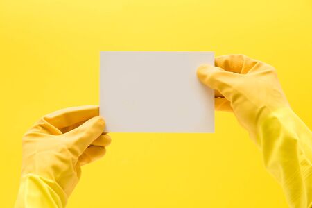 hand in a yellow cleaning glove holing a blank white card