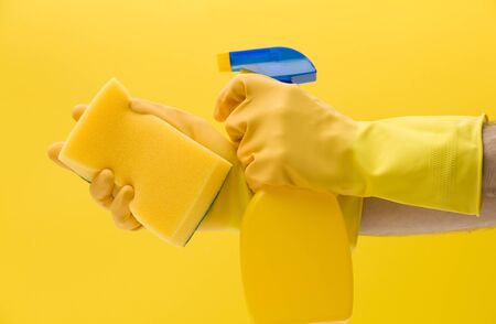 Hand wearing a yellow rubber glove holding a cleaning sponge and spray bottle