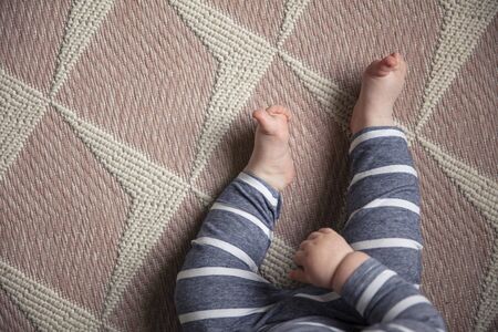 Overhead view of cute babies legs and toes sat on a pink nursery rugの写真素材