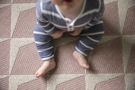 A baby in blue clothes sitting on a rug at home shot from overheadの写真素材