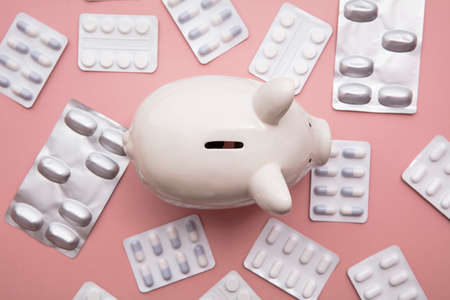 Healthcare cost. Money box piggy bank with packets of pills and tabletの写真素材