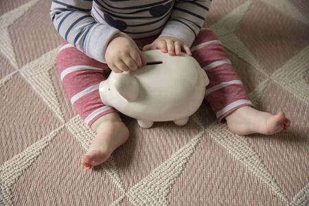 A baby puts money into a piggy bank saving for their futureの写真素材