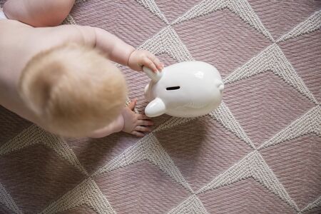 Overhead view of a baby reaching for a piggy bank savings boxの写真素材