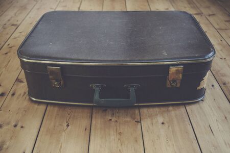 An old vintage brown travel suitcase on a wooden floorの写真素材