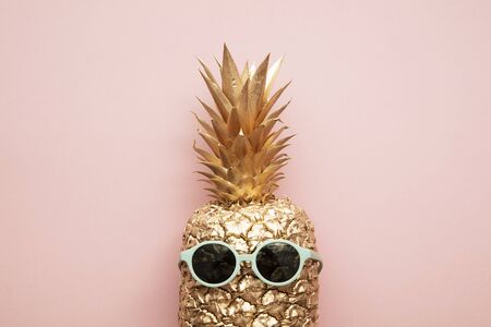 Gold trendy pineapple wearing summer sunglasses on pink