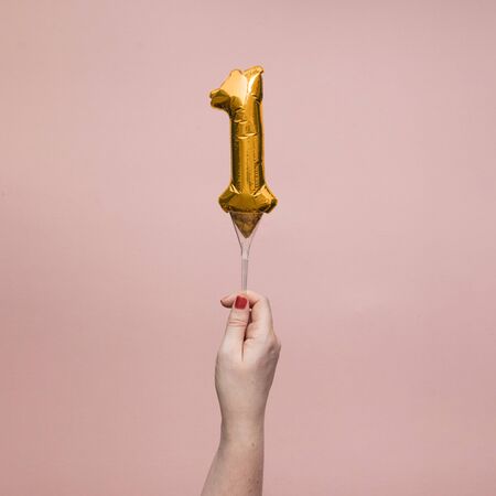 Female hand holding a number 1 birthday anniversary celebration gold balloon.