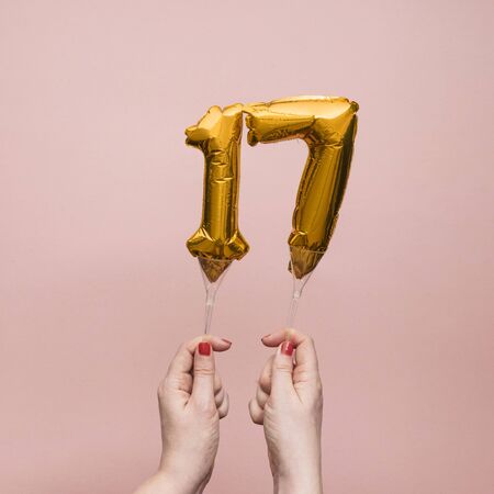 Female hand holding a number 17 birthday anniversary celebration gold balloon.