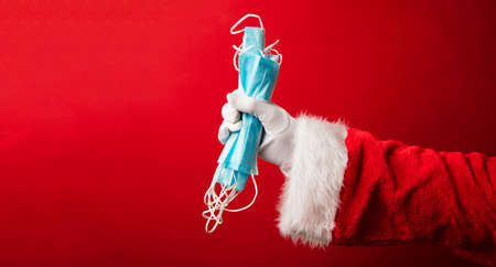 Santa Claus hands holding a coronavirus surgical face mask. Covid Christmasの写真素材