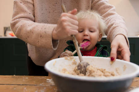 Mum and son baking cakes together. Child licking a spoon.の写真素材