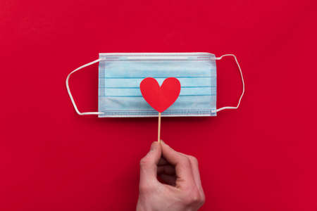 Hand holding a red love heart over a protective face mask.の写真素材
