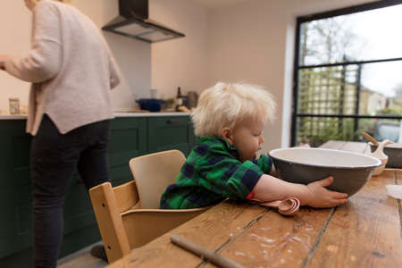 A toddler helping with the baking in he kitchen holding a mixing bowl.の写真素材