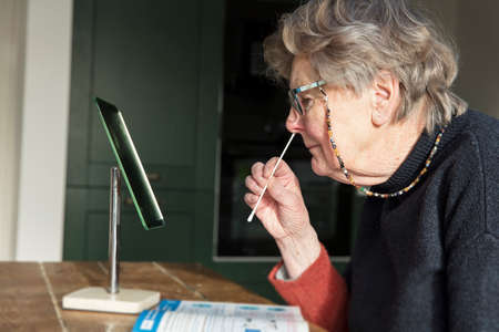 A woman looing in a mirror taking a covid-19 home testing nasal swab