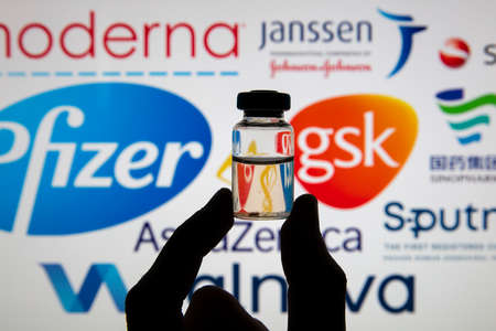 OXFORD, UK - February 2020: Vaccine dose bottle infront of Covid vaccine logos