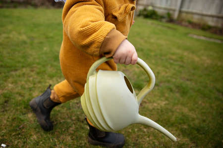 A young child helping out in the garden watering plants with a watering can