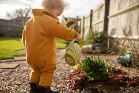 A young child helping out in the garden watering plants with a watering can