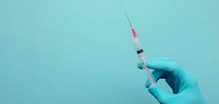 A doctor or nurse wearing blue surgical gloves holding a vaccine syringe