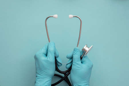 A doctor wearing blue surgical gloves holding a medical stethoscopeの写真素材