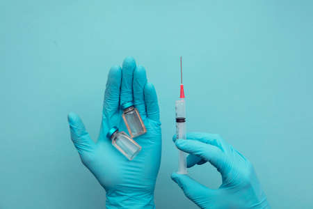 Doctor or nurse wearing blue surgical gloves holding a syringe and vaccine doseの写真素材