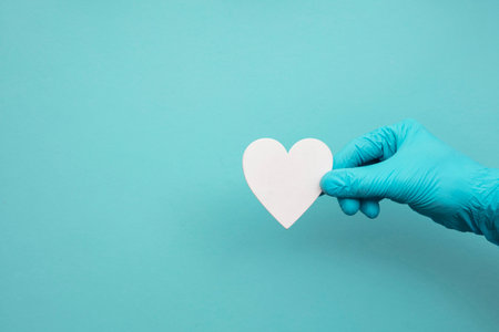 Doctors hands wearing blue surgical gloves holding a white heart shapeの写真素材