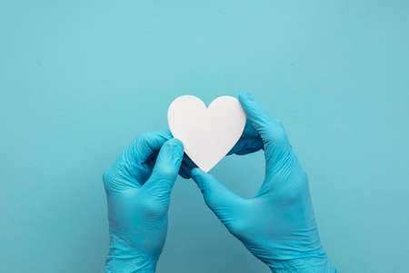 Doctors hands wearing blue surgical gloves holding a white heart shape