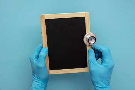 Doctor in blue surgical gloves holding a blank chalkboard.の写真素材