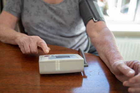 An older senior woman checks her blood pressure at home. Health care concept