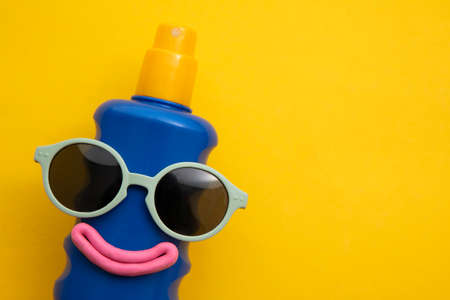 Happy sun block bottle wearing sunglasses and a smile on a yellow background