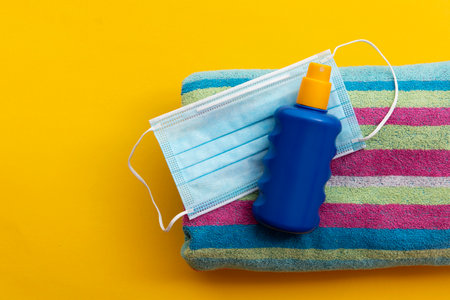 protective face mask and suncream on a summer vacation beach towel