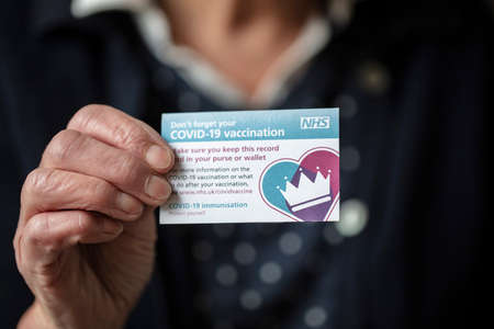LONDON, UK - APRIL 2021. A person holding NHS Covid-19 vaccination record cardのeditorial素材