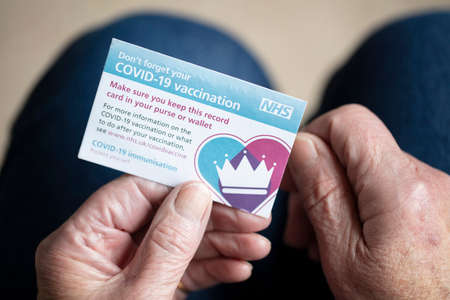 LONDON, UK - APRIL 2021. A person holding NHS Covid-19 vaccination record cardのeditorial素材