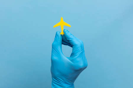 A person wearing a medical surgical glove holding a yellow travel airplaneの写真素材
