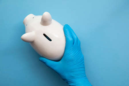 Doctor wearing blue gloves holding a piggy bank. Health care finance conceptの写真素材