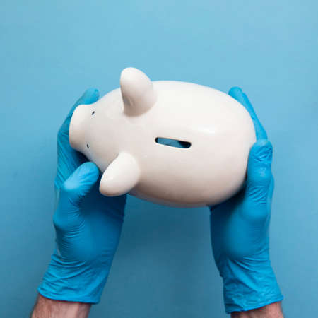 Doctor wearing blue gloves holding a piggy bank. Health care finance conceptの写真素材