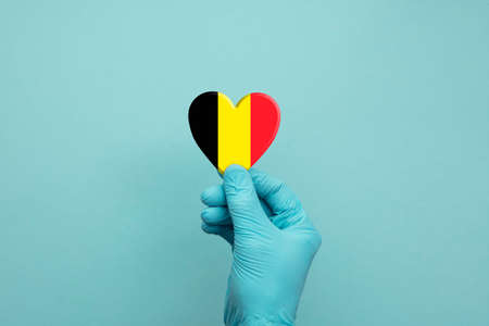 Hands wearing protective surgical gloves holding Belgium flag heartの写真素材