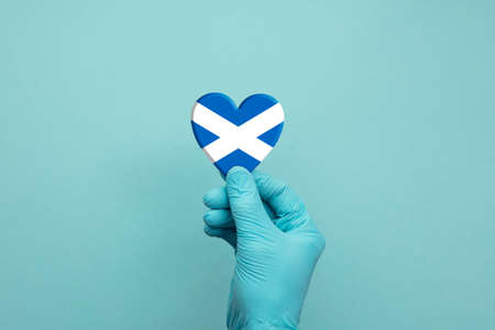 Hands wearing protective surgical gloves holding Scotland flag heartの写真素材