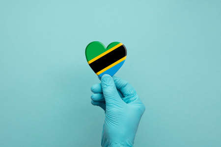 Hands wearing protective surgical gloves holding Tanzania flag heart