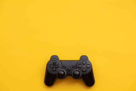 Black video game controller on a bright yellow backgroundの写真素材