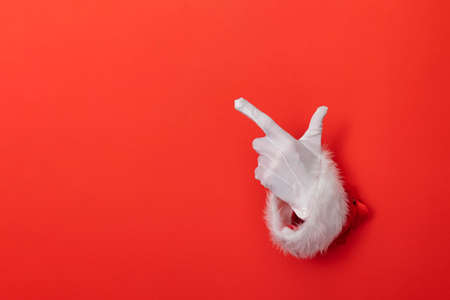 Santa Claus hand pointing through a hole in red paper background