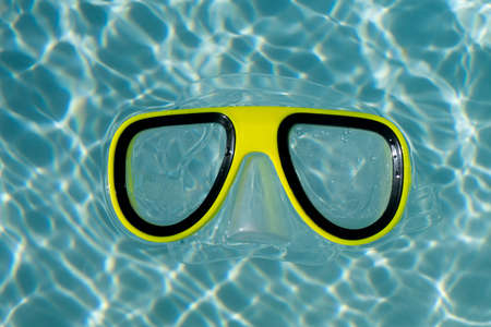 A yellow snorkel swimming goggles floating in a clear blue rippled swimming poolの写真素材
