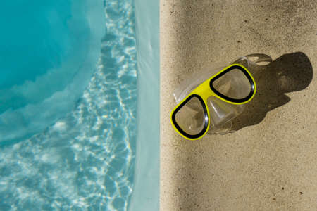 Yellow swimming goggles next to a clear blue rippled swimming poolの写真素材