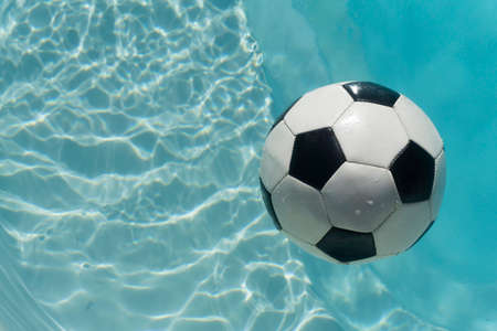 Black and white soccer football floating in a blue clear swimming pool. Summer sport backgroundの写真素材