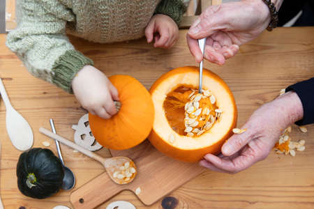 orange Halloween pumpkin being carved into a lantern decoration by a grandmother and childの写真素材
