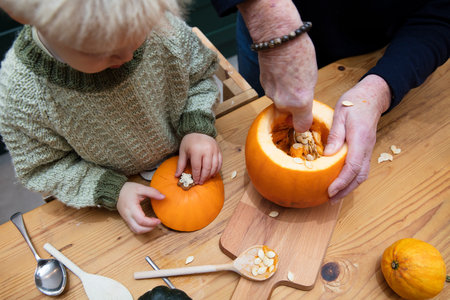 A toddler and Grandmother carve a halloween pumpkin decoration togetherの写真素材