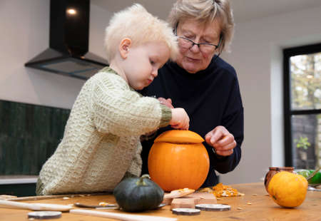 A toddler and Grandmother carve a halloween pumpkin decoration togetherの写真素材
